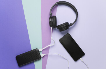 Power bank charges a smartphone and wireless headphones on a pastel background