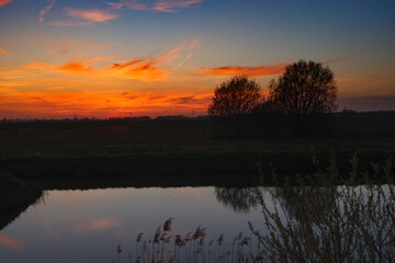Obraz premium Evening sunset over a lake with trees and clouds in the sky, capturing nature's scenery and reflection in still water