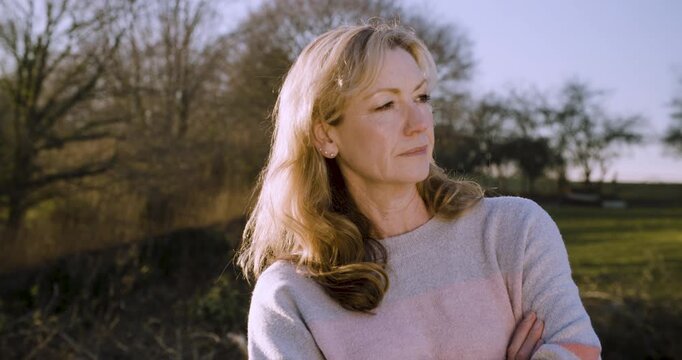 Attractive happy middle aged woman in her forties outside looking thoughtful, smiling and folding her arms