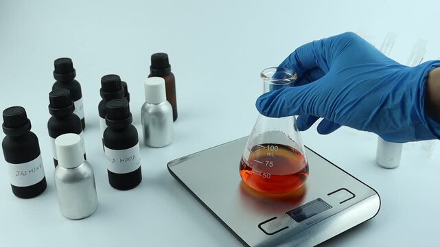 chemical beaker , flask is on digital scale white table with blotting paper , fragrance bottle and essential oil bottle used to blend nice scent for making perfume and candle by perfumer in laboratory