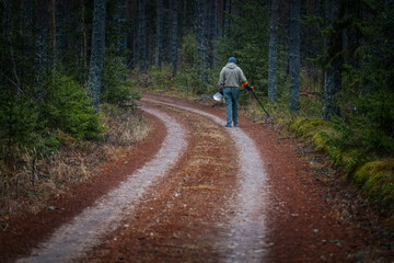 Obraz premium Individual walking along a winding forest path, holding a tool for maintenance, surrounded by tall trees and earthy tones, showcasing nature's tranquility and outdoor activity