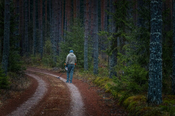 Obraz premium Man walking along a winding dirt path through a dense forest, surrounded by tall trees and lush greenery, showcasing the beauty of nature and outdoor exploration