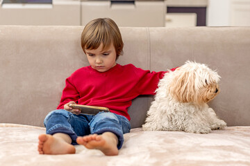 Little boy watching cartoon on smartphone with his dog on the couch