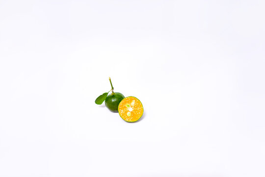 Fresh green Kasturi oranges on a white backdrop. One sliced half reveals a juicy orange pulp with seeds. Minimalist, vibrant, and detailed citrus fruit images