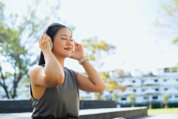 Fototapeta premium Beautiful Asian woman in sportswear with headphones smiling and enjoying fresh air in green park, relaxing feeling peaceful, energetic and alive in healthy outdoor lifestyle