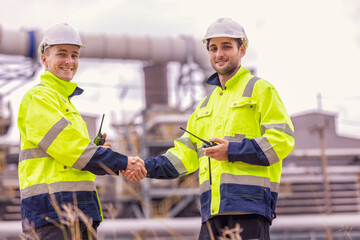 Industrial engineer, workers in a refinery - oil processing equipment and machinery energy factory. Image of engineers handshake as symbol of their success partnership. Teamwork successful concept.