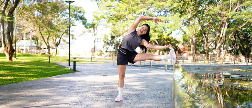 Healthy young Asian runner woman warm up the body stretching before exercise at park under warm light morning. Lifestyle fitness and active women exercise in urban city concept.