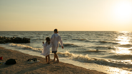 Two young children, a brother and sister, walk hand in hand along a sun-drenched sandy beach during...