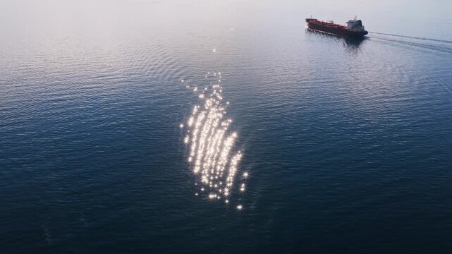 Aerial drone view of an oil tanker traveling across open Adriatic waters with distant mountain ridges and coastal towns visible on the horizon. Water sparkling reflection