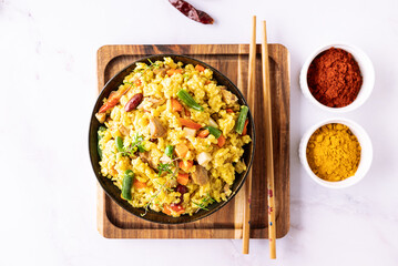 Stewed rice with meat and assortment on vegetables and spices in dark ceramic bowl on white marble table top view. Tasty homemade food concept.