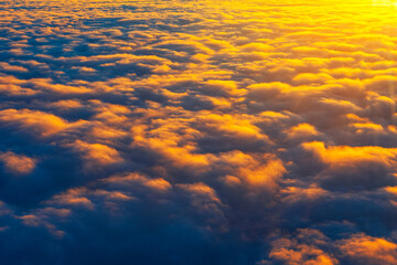 Golden sunlight bathes cloud tops in a warm glow, casting dramatic shadows across the dense formations. Aerial view captures nature serene beauty and the ethereal texture of the sky