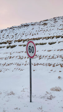 Frozen road sign covered with ice and snow in a winter landscape. The scene shows hazardous driving conditions in cold weather, suitable for themes of road safety, winter travel, and climate