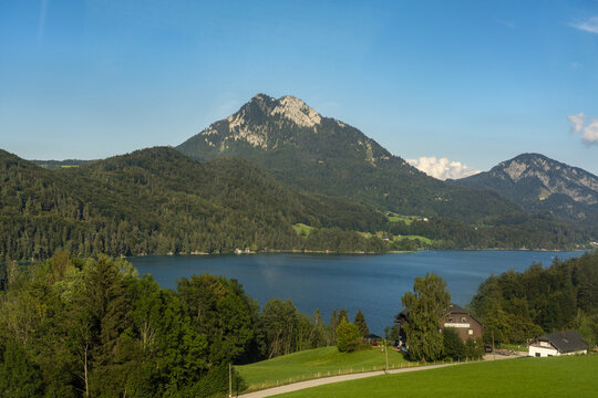 Aerial view of the serene Fuschlsee lake mirroring the lush green slopes and the towering Schafberg mountain under a clear blue sky, Fuschl lake, Salzburg, Austria.