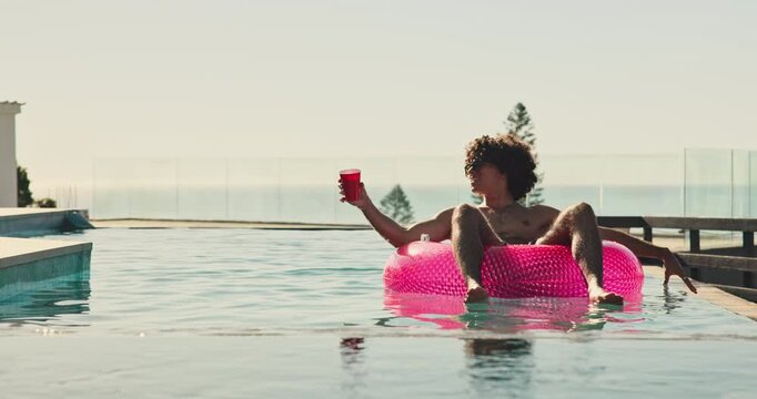 Float, drink and man in pool at holiday home for relax in summer on vacation or weekend trip. Dancing, calm and male person on inflatable with alcohol beverage in water for sunbathing at resort.