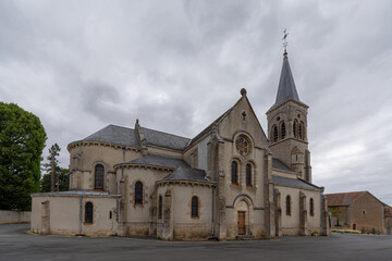 Obraz premium Side view of Église de Sainte-Sévère-sur-Indre, highlighting its stone walls, Gothic windows, and bell tower beneath a dramatic cloudy sky.