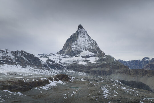 Aerial view of the majestic Matterhorn peak piercing through the clouds, its snow-dusted slopes contrasting with the rugged terrain below, Zermatt, Valais, Switzerland.
