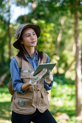 Female Asian botanical researcher studies plant life with digital tablet in vibrant green natural forest environment for ecological analysis