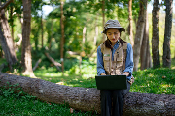 Fototapeta premium Adult Asian woman botanist conducts field research using laptop outdoor explore nature document findings scientific study forest environment