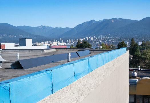Roof metal flashing installation on flat roof with defocused city and mountains. 2-ply SBS or modified bitumen roofing repair. Waterproof membrane and sheet metal corner installation. Selective focus.