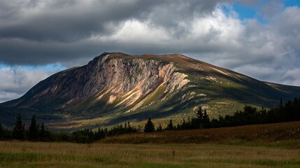 Dramatic landscape of a mountain under a cloudy sky, with hints of autumn foliage