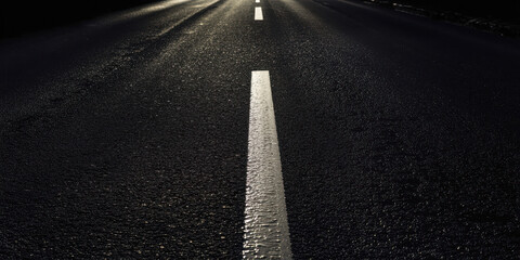 wet asphalt road with white center line leading to bright distant light on dark night background