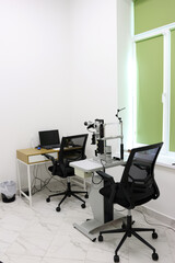 Interior of an ophthalmologist's office with a slit lamp biomicroscope, a table with a laptop in a bright and clean medical examination room.