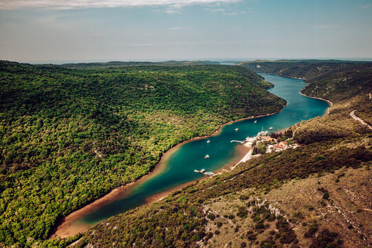 Aerial view of the winding river cutting through the lush green landscape, with boats dotting the water near the shore, Pican, Istria County, Croatia.