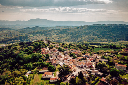 Aerial view of the town nestled among rolling hills with the church steeple piercing the sky, the terracotta roofs contrasting with the lush greenery, Pican, Istria County, Croatia.