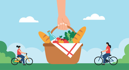 Hand holding a large picnic basket overflowing with food while people cycle through a sunny park in the background.