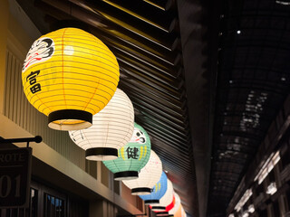 Traditional Japanese Daruma paper lanterns hanging in a row at night with warm glowing light.