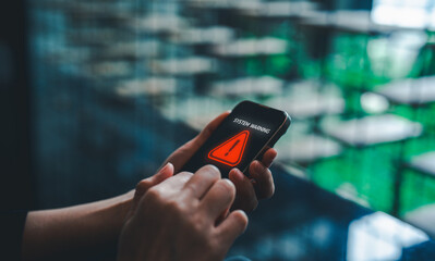 A person holding a smartphone displaying a system warning alert on the screen, set against a blurred, modern background.