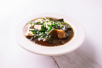 Fresh traditional miso soup with tofu, shiitake mushrooms, green onion, sea mustard and spices on white background with copy space for your design. Traditional Japanese cuisine. 