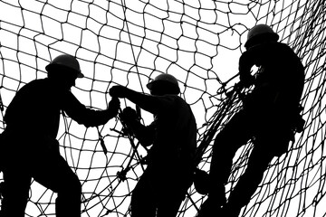 Teamwork and Precision: Silhouette of construction workers collaborating on intricate net installation. They demonstrate careful precision. 