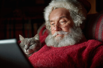 Santa Claus sitting with cat and using tablet.