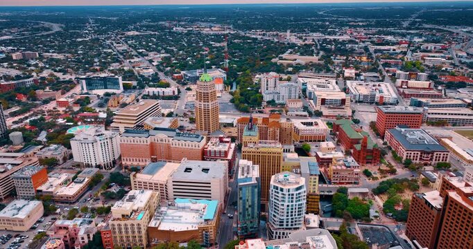Flying closer to the Tower Life Building with a flag on top. Vast scenery of San Antonio, Texas with lush greenery.