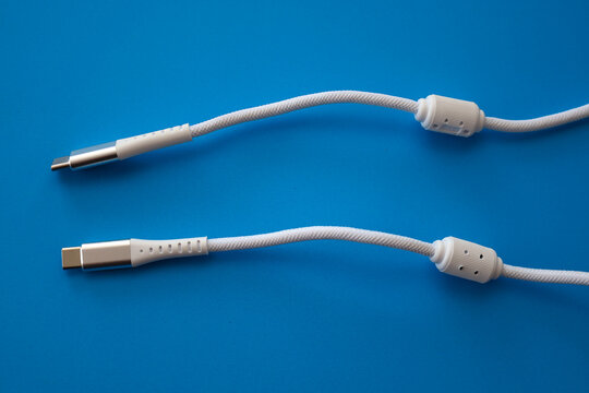 Two white USB Type-C cables in a durable textile braid with ferrite filters are symmetrically arranged on a bright blue background.