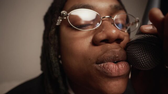 Close up shot of fashionable young African American man wearing silver gills rapping in microphone with passion recording new track in studio, soft vignette effect