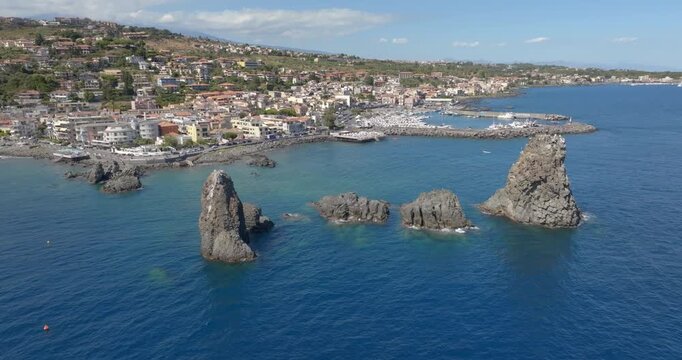 Aerial view of the town of Aci Trezza overlooking the Ionian Sea, in province of Catania, Sicily, Italy. In the foreground, off the coast, there are three tall, characteristic and prominent sea stacks