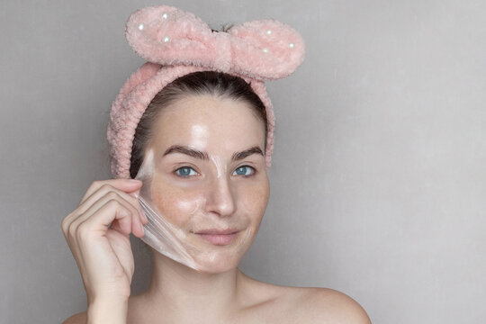 Caucasian woman makes a cosmetic Peel Off Mask. She removes the film mask with her hand copy space photo