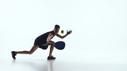 Female padel player moving forward and reaching ball in studio. Concept of digital speed processing, reaction systems, real time analytics and padel performance platforms.