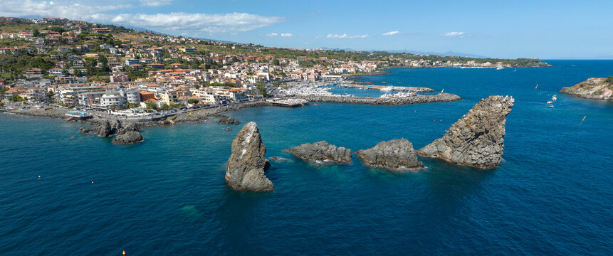 Panoramic aerial view of Aci Trezza, in the province of Catania, Sicily, Italy. It is a tourist resort on the Mediterranean Sea. In the foreground are the Cyclopean Isles. It is a sunny day morning.