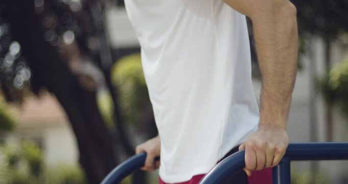 
 Athlete performs dips exercise outdoors, street workout, middle close-up, slow motion