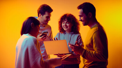 Colleagues reviewing data together on laptop and tablet under neon light. Concept of team analytics, business review, performance evaluation, reporting process and collaborative problem solving.