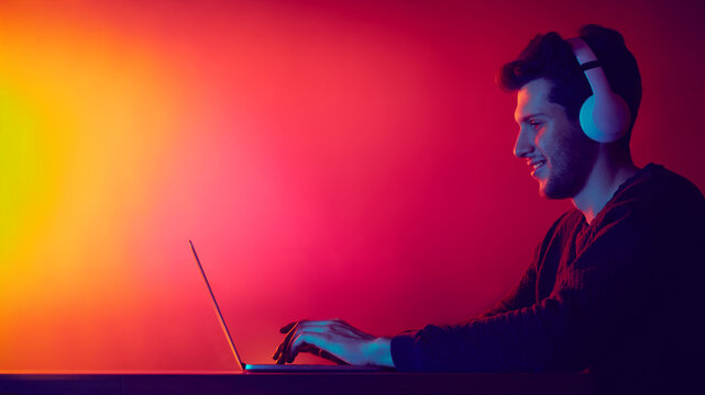 Man using laptop with headphones in neon digital environment. Concept of focused workflow, online meetings, remote communication and technology powered concentration. - Powered by Adobe