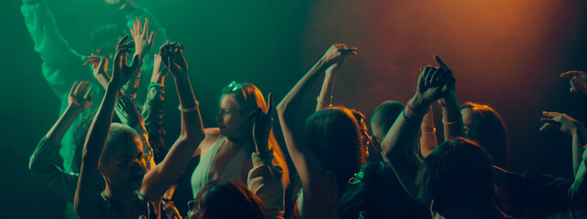 Crowd dancing in dramatic light with raised hands. Concept of collective expression, emotional freedom, music immersion, shared movement and Christmas nightlife celebration. Banner © master1305
