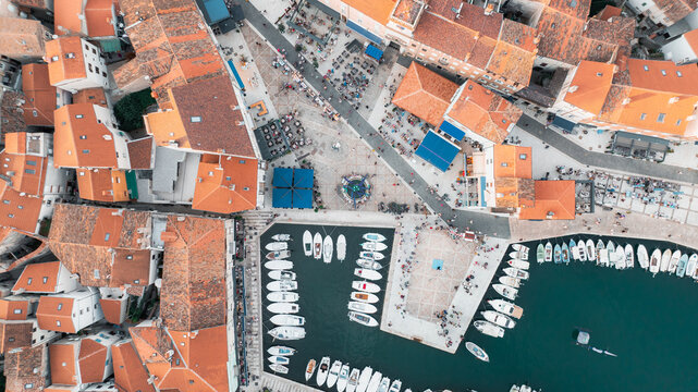 Aerial view of a harbor filled with boats contrasting against the terracotta rooftops and bustling Riva creskih kapetana, Cres, Primorsko-goranska zupanija, Croatia.