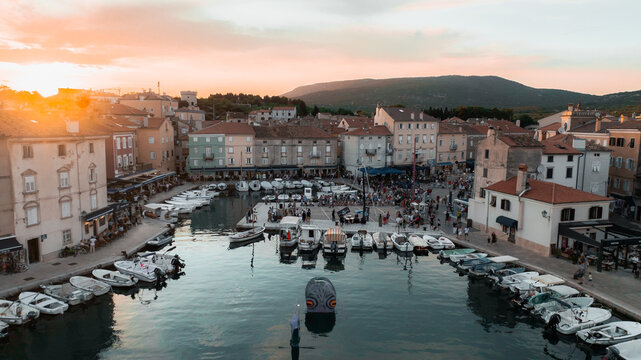 Aerial view of boats nestled in the harbor, framed by historic buildings under a warm sunset glow, Ulica Riva creskih kapetana, Cres, Primorsko-goranska zupanija, Croatia.