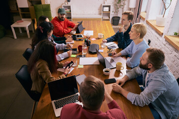 Creative team meeting viewed from above in modern office. Concept of strategic discussion, collaborative planning, teamwork dynamics and contemporary coworking business environment.