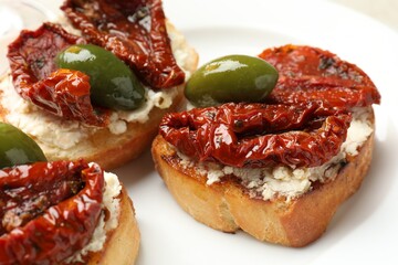 Delicious bruschettas with cream cheese, sun-dried tomatoes and green olives on plate, closeup