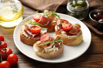 Delicious bruschettas with cream cheese, prosciutto, tomatoes and arugula on wooden table, closeup